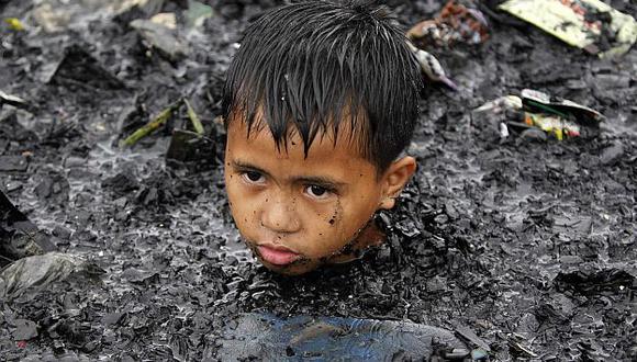 Un niño filipino con el lodo hasta el cuello busca objetos de valor tras inundaciones. (Reuters)