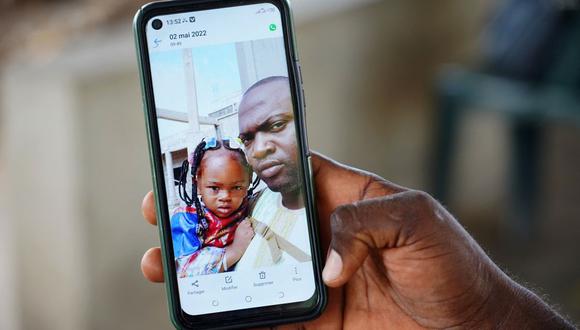 Wuri Bailo Keita, de 33 años, sostiene un teléfono móvil que muestra una foto de él y su difunta hija, Fatoumatta, quien se cree que murió de insuficiencia renal aguda, en Banjul el 10 de octubre de 2022. (Foto de MILAN BERCKMANS / AFP)