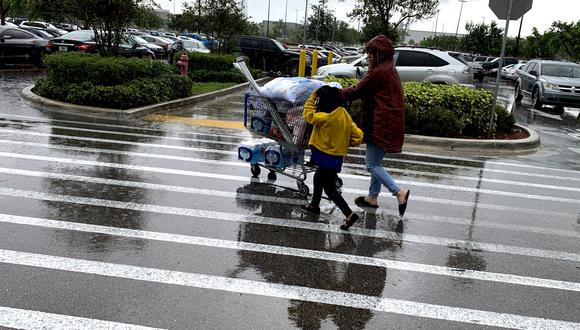 Una mujer y un niño tiran de un carrito con víveres afuera de Walmart durante una ráfaga de viento del huracán Dorian. (Foto: AFP)