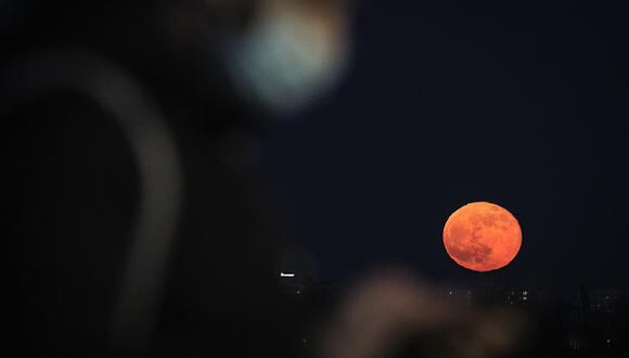 A man wearing a face mask is seen with the Pink Super Moon rising in the background Warsaw, Poland on April 27, 2021. The Pink Super Moon is second to last super moons in 2021. (Photo by STR/NurPhoto via Getty Images)