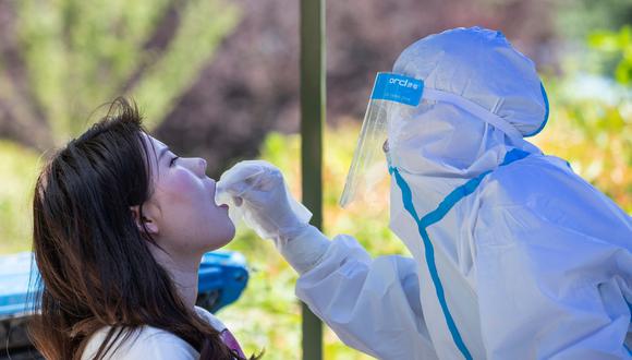 Un trabajador de salud realiza una prueba de coronavirus a una mujer en la Universidad de Wuhan. (Foto: China OUT/AFP).