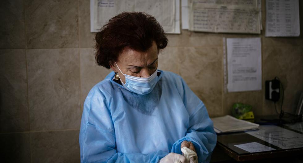Esta fotografía tomada el 20 de enero de 2021 muestra a la doctora Maria Bogoeva, de 82 años, especialista búlgara en enfermedades infecciosas, quitándose los guantes quirúrgicos durante su turno en una unidad COVID-19 en el hospital de Doupnitsa. (Dimitar DILKOFF / AFP).