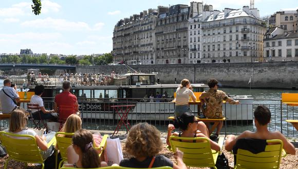 La gente descansa en un paseo marítimo mientras un bateau-mouche (barco turístico) navega por el río Sena durante el evento anual de verano Paris-Plage (playa de París) en París el 9 de julio de 2022 (Foto de ALAIN JOCARD / AFP)