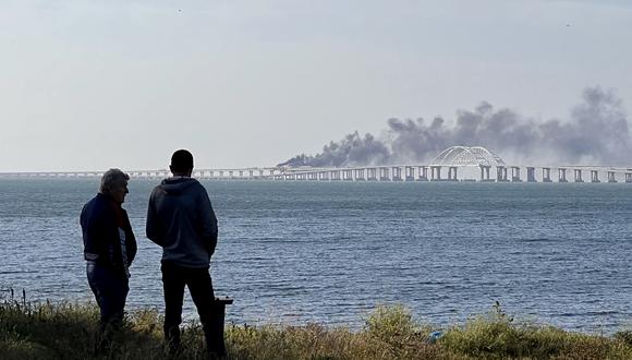 La gente mira el espeso humo negro que se eleva desde un incendio en el puente de Kerch que une Crimea con Rusia, luego de que explotara un camión, cerca de Kerch, el 8 de octubre de 2022. (Foto: Roman DMITRIYEV / AFP)