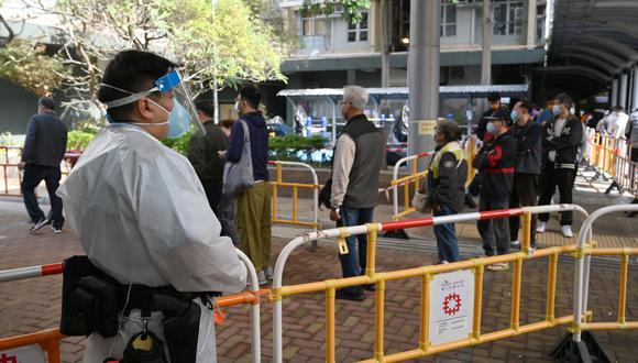 Un policía con ropa protectora hace guardia mientras los residentes hacen cola para hacerse las pruebas de covid en la urbanización Kwai Chung en Hong Kong, el 27 de enero de 2022. (Foto de Peter PARKS / AFP)