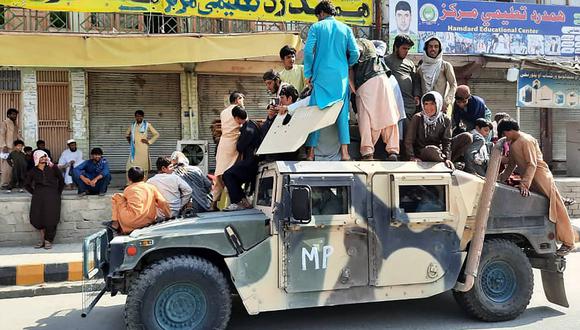 Los combatientes talibanes y los residentes locales se sientan junto a un vehículo Humvee del Ejército Nacional Afgano (ANA) a lo largo de la carretera en la provincia de Laghman el 15 de agosto de 2021. (AFP)