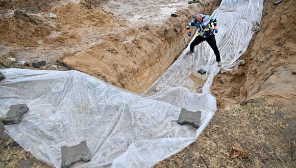 A communal worker removes the plastic covers from a mass grave in Bucha, near Kyiv on April 9, 2022. (Photo by Sergei SUPINSKY / AFP)