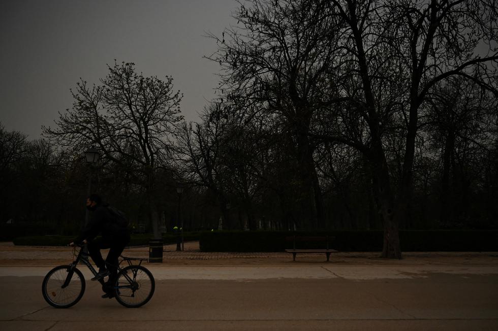 Un ciclista monta su bicicleta mientras la arena del Sahara que cayó durante la noche cubre la carretera en el parque del Retiro en Madrid el 15 de marzo de 2022. - Este fenómeno meteorológico, fuertes vientos calientes cargados de polvo de arena del desierto del Sahara, se llama en España el "calima". (Foto de Gabriel BOUYS / AFP)