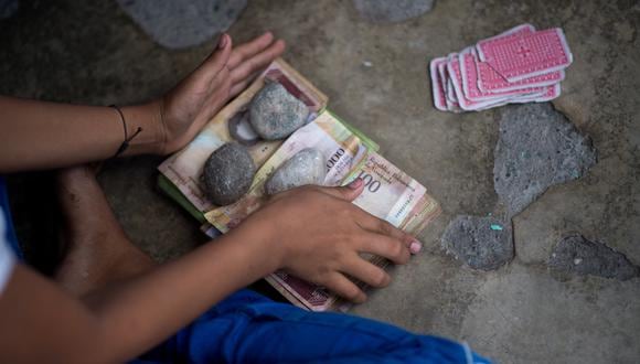Los niños juegan a las cartas y apuestan con billetes de bolívares venezolanos no utilizados en una calle del pueblo de Puerto Concha, estado Zulia. (Foto: Federico PARRA / AFP)
