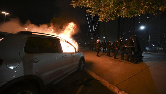 La policía antidisturbios toma posición junto a un vehículo en llamas luego de los enfrentamientos con simpatizantes del presidente Jair Bolsonaro que protestaban por el arresto de un líder indígena en Brasilia el 12 de diciembre de 2022. (Foto de EVARISTO SA / AFP)