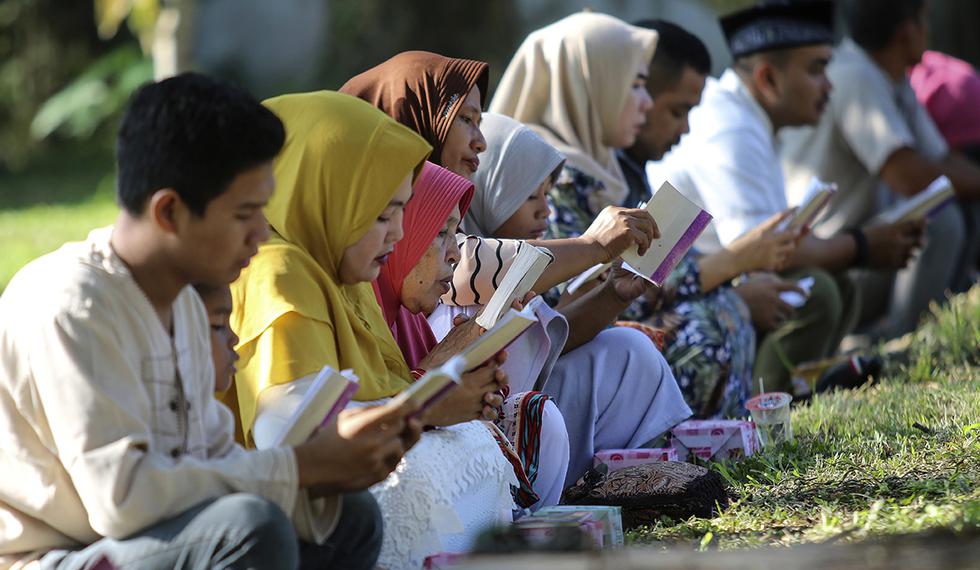 La gente lee el libro sagrado del Corán mientras rezan en una fosa común por las víctimas del tsunami del Océano Índico, durante la conmemoración del 15 aniversario del desastre en Banda Aceh, Indonesia. (Foto: AP)