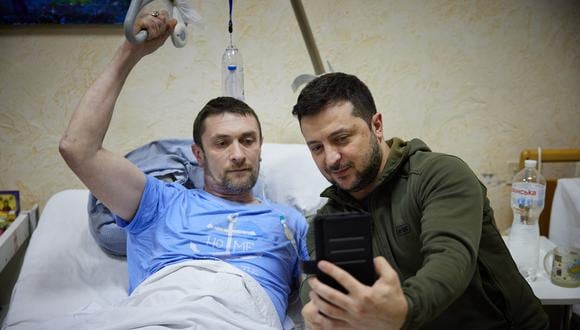 El presidente de Ucrania, Volodymyr Zelensky  se toma una selfie con un hombre herido acostado en una cama durante una visita a un hospital militar luego de los combates en la región de Kiev. (Foto: UKRAINIAN PRESIDENTIAL PRESS SERVICE / AFP)