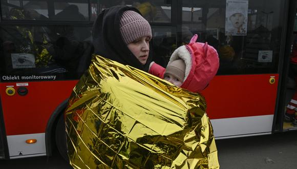 Una mujer con su hijo espera en temperaturas heladas para subirse al autobús, después de cruzar la frontera de Ucrania con Polonia, en el cruce fronterizo de Medyka en Polonia, el 7 de marzo de 2022. (Foto: Louisa GOULIAMAKI / AFP)