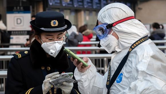 Un personal de seguridad con ropa protectora habla con un miembro del personal del metro con una máscara en la entrada de una estación de metro en Beijing. (Foto: AFP)