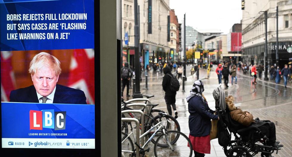 Una pantalla de noticias muestra al primer ministro británico, Boris Johnson, mientras los compradores recorren las calles de Manchester, noroeste de Inglaterra, el 13 de octubre de 2020. (AFP / Oli SCARFF).