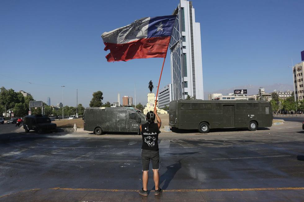 Un hombre hondea una bandera mientras pasan camiones de carabineros durante una nueva protesta en contra del gobierno del presidente de Chile, Sebastián Piñera. (EFE/Elvis González).