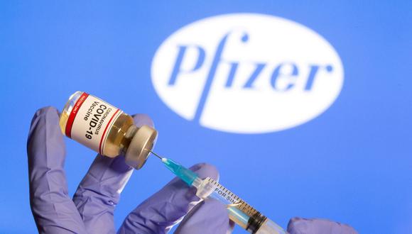 Una mujer sostiene una pequeña botella etiquetada con una etiqueta de "Vacuna contra el coronavirus COVID-19" y una jeringa médica frente al logotipo de Pfizer que se muestra en esta ilustración. (REUTERS / Dado Ruvic).