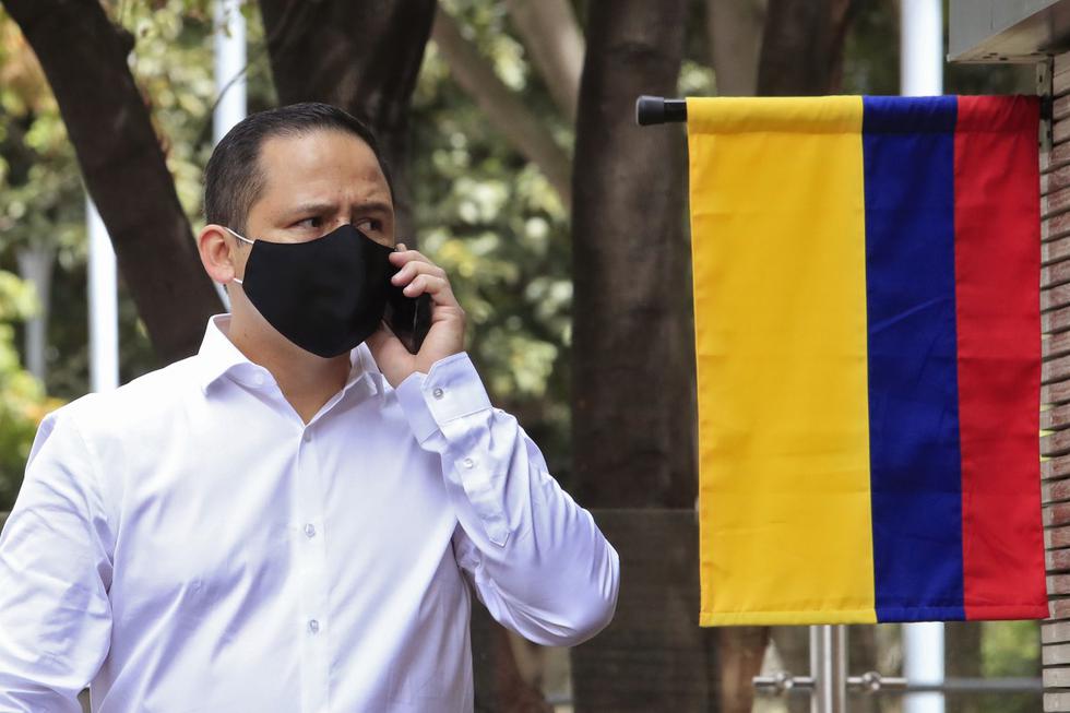 Un hombre que usa una mascarilla por el coronavirus y habla por su teléfono móvil pasa junto a una bandera de Colombia en Bogotá. (DANIEL MUNOZ / AFP).