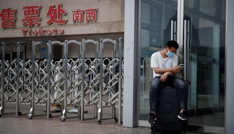 Un hombre usa una máscara protectora contra el coronavirus mientras está sentado en su maleta en la estación de tren oeste de Beijing (China). (REUTERS/Thomas Peter).