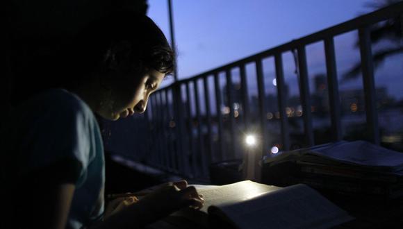 Alana Rivera, de 10 años, hace su tarea diaria en el balcón de su apartamento iluminado por la luz de un teléfono celular en San Juan, Puerto Rico, el 6 de noviembre de 2017. (Ricardo ARDUENGO / AFP).