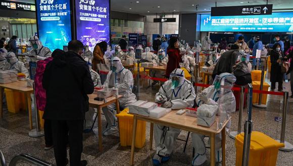 Trabajadores de la salud esperan para hacer la prueba del coronavirus a los pasajeros después de su llegada a la estación de tren de Hongqiao en Shanghái, el 6 de diciembre de 2022. (Foto de Hector RETAMAL / AFP)
