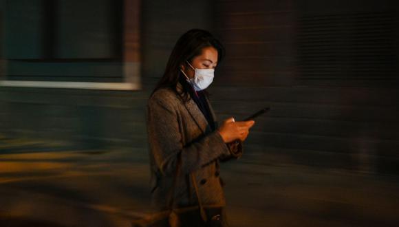 Una mujer usa una máscara facial en medio de preocupaciones por la propagación del coronavirus COVID-19 mientras revisa su teléfono celular en Shanghái el 17 de marzo de 2020. (Foto de Hector RETAMAL / AFP)